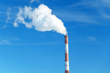 Smokestack emits thick smoke from a pipe, contrasting against a clear blue sky