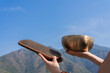 A girl holds Sadhu boards and a Tibetan singing bowl against the background of the blue sky and the Himalayas.