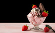 Strawberry ice cream sundae with fresh strawberries and dark chocolate pieces in a glass bowl, with copy space..
