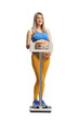 Pregnant woman in sportswear holding her belly and standing on a medical weight scale