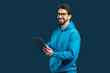 © Prostock-studio - A man wearing a blue hoodie is holding a tablet device in his hands. He appears focused on the screen, possibly scrolling or interacting with the tablet.