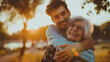 © MYDAYcontent - A man embraces a old mother woman warmly in a park setting, expressing love and affection during sunset.