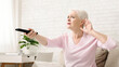 Senior woman cupping her hand behind ear to hear better to the television, making sound louder, empty space