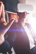 Young woman in suit wearing virtual reality headset in airplane and gesturing with hands to control simulation of 3D futuristic dimension.Contemporary advanced technology and innovation. Female use VR