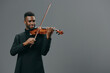 Talented young African American man in a black suit playing the violin on a grey background