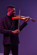 Talented young African American man playing violin with passion on vibrant purple background, artistic music performance concept