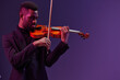 Professional musician playing the violin in elegant black suit on vibrant purple background