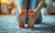 Close-up photo of a female's feet soles. A woman is sitting on the floor at home, massaging her feet with her fingers. Her nicely manicured fingers relieve legs' pain.