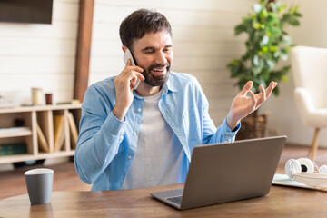 Aufkleber - A man is multitasking as he talks on a cell phone and works on a laptop simultaneously. He appears focused and engaged in his tasks, showing efficient use of technology in a modern workspace.