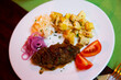 Plate with a meat dish lula-kebab, stewed potatoes, pickled cabbage, onions and slices of fresh tomato.