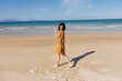 Woman in Yellow Dress Standing on Beach with Ocean in Background Against Clear Blue Sky on Sunny Day