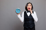 Fototapeta Tulipany - Anxious asian waitress panicking while holding circle dial alarm clock and looking at camera with open mouth. Young terrified woman receptionist showing timer watch portrait