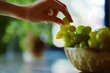 Person reaching for fresh grapes in a bowl with a plant in the background