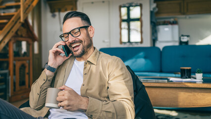 Wall Mural - One adult man sit at home talk on mobile phone and hold cup of coffee