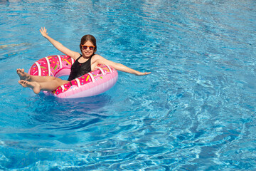 Smiling cute little girl wearing sunglasses in the pool on a sunny day