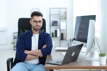 Happy young programmer working with laptop in office
