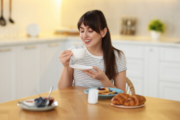 Wall Mural - Smiling woman drinking coffee at breakfast indoors