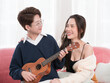© panyajampatong - Young Asian lesbian couple intending to play a musical instrument together, guitar and kalimba, in the living room at home, the lifestyle of couple LGBT loving women happy in romantic love and fun