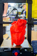 3D printer and model of human heart printed on 3D printer. Red prototype of human heart printed on 3D printer on a 3D printer desktop. New modern additive printing medical healthcare technologies