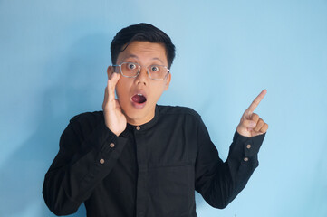 Handsome Asian man in black shirt is pointing his finger to the up at an empty space. showing option, recommendation, presentation