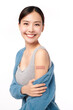 young asian women smiling after getting a vaccine, holding down her shirt sleeve and showing her arm with bandage after receiving vaccination on white background,