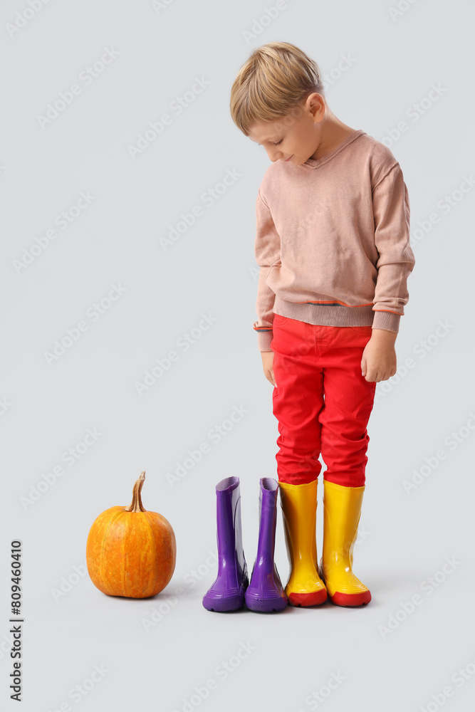 Little boy with rubber boots and pumpkin on light background