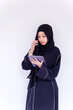 Muslim student wearing Abaya niqab traditional clothes standing review the lesson on tablet for the exam in university on white wall background.