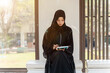 Asian Muslim wearing traditional clothes sit and review the lesson on tablet for the exam in university with sun fare and blurred background.