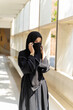 A Muslim student wearing traditional clothes and pull the cloth over your face as is customary in Islam on walkway at her school building with sun flare background.