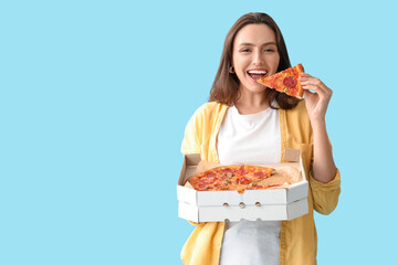 Poster - Young woman eating piece of tasty pizza and holding cardboard box on blue background