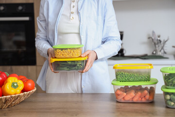 Wall Mural - Woman holding plastic containers with frozen vegetables at table in kitchen