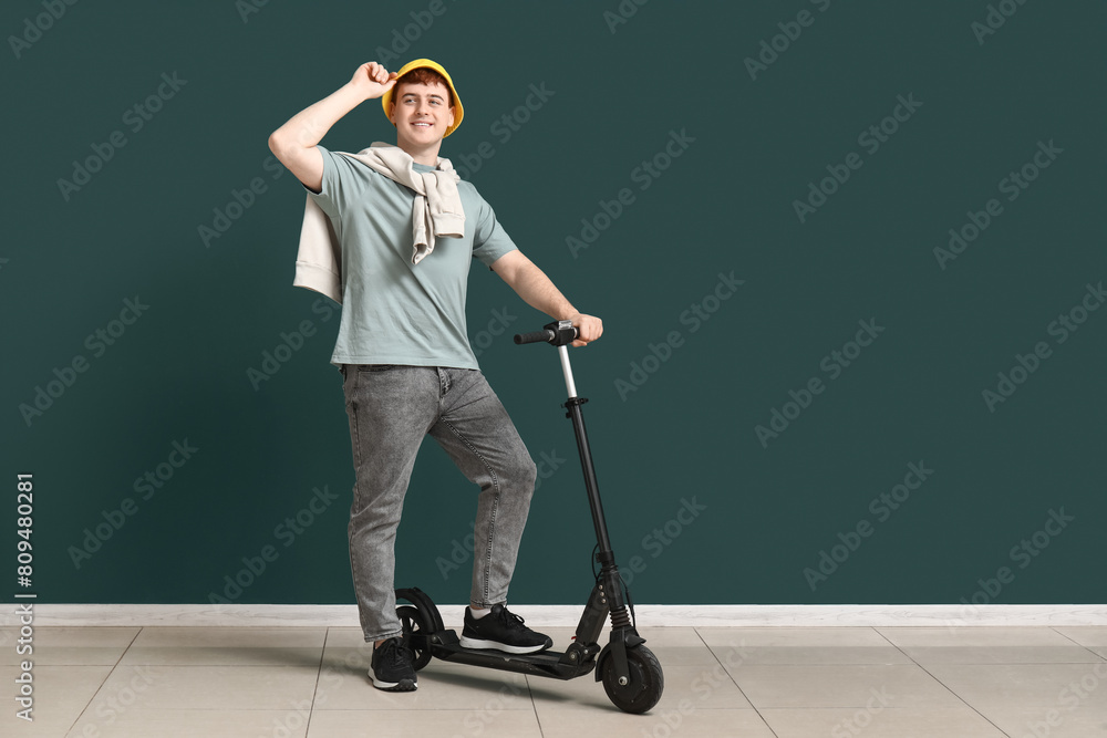 Young man with modern electric kick scooter near green wall