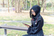 Young Asian beautiful woman Muslim medical student wearing traditional clothes relaxing with tablet in the hospital park with sun fare and blurred background.