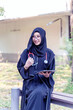 Young beautiful woman Asian Muslim medical student wearing traditional clothes relaxing with tablet in the hospital park with sun fare and blurred background.