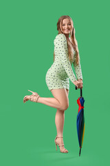 Poster - Beautiful young happy woman in stylish dress with umbrella on green background