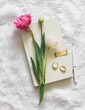 Tulips, a book, earrings, a pen on white sheets top view. Aesthetic still life