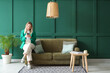 © Pixel-Shot - Young woman using mobile phone on sofa in green living room