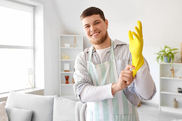 Poster - Young bearded man putting on rubber glove before cleaning at home