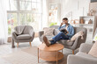 © Pixel-Shot - Young tattooed man in headphones reading magazine on sofa at home
