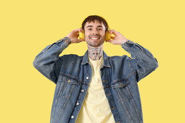 Wall Mural - Young tattooed man in headphones listening to music on yellow background