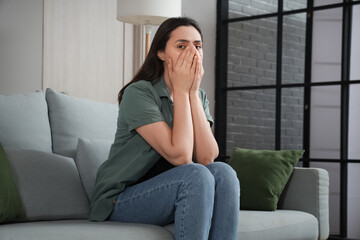 Poster - Depressed young woman sitting on sofa at home