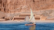 Beautiful Nile scenery with traditional Felluca sailing boat in the Nile Hatshepsut Temple at sunrise in Valley of the Kings and red cliffs western bank of Nile river - Luxor- Egypt