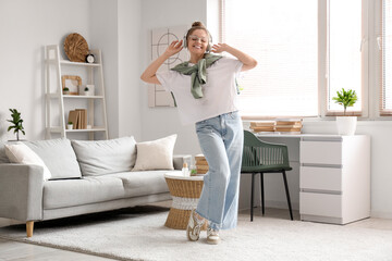 Wall Mural - Young woman in eyeglasses and headphones dancing near sofa in living room