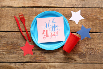 Wall Mural - Composition with dinnerware, greeting card for Independence Day celebration and paper stars on wooden background