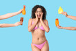 © Pixel-Shot - Surprised young African-American woman in swimsuit and hands with bottles of sunscreen cream on blue background