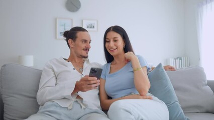 Wall Mural - Caucasian young couple sitting on sofa and swipe mobile phone in house. 