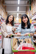 Two happy young Asian women shop together in a grocery store, walking with a shopping cart.