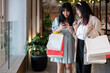 Two Asian women stand together in a shopping mall corridor, looking at a smartphone.