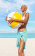 Smiling girl at the beach side holds inflatable beach ball, wearing a bikini and pareo, African latin American woman. Concept of a seaside holiday or shopping for a summer beach holiday