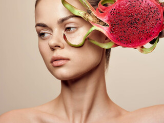 Beautiful young woman with dragon fruit on her head in closeup on beige background, exotic and vibrant fruit concept